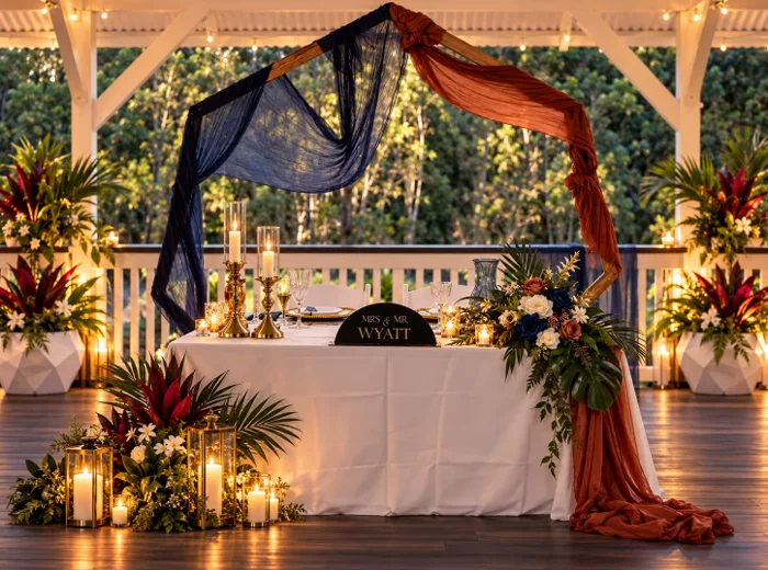 Sweetheart table with navy and rust draping, candles and tropical florals